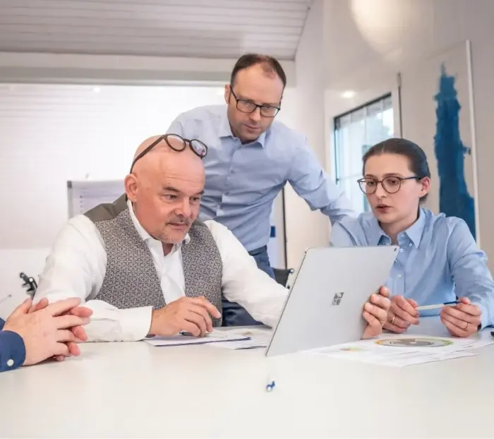 Zwei Männer und eine Frau sitzen um einen Laptop und diskutieren interessiert miteinander.