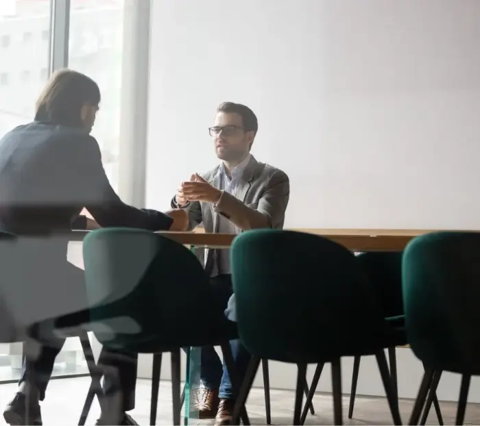 Zwei Männer sitzen sich an einem Bürotisch gegenüber und diskutieren miteinander.