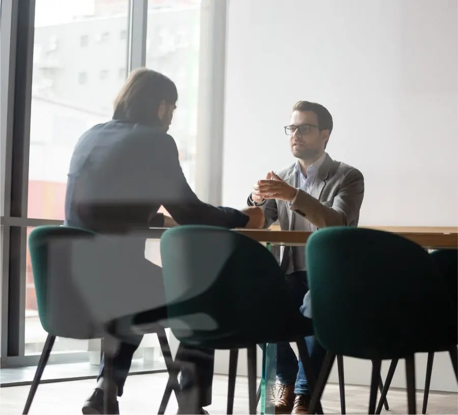 Zwei Männer sitzen an einem Tisch in einem Büro und führen ein Gespräch.