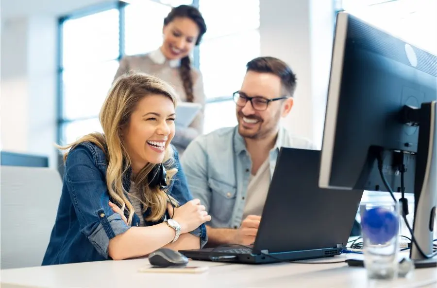 Eine Frau und ein Mann sitzen lachend vor einem Computer.