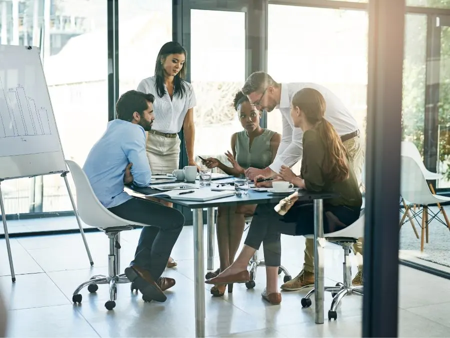 Fünf Personen sitzen um einen Tisch in einem Büro und diskutiert gemeinsam.