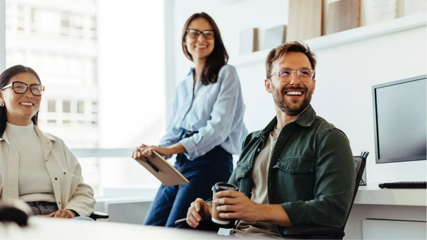 Drei Personen in einem Büro blicken lachend seitlich aus dem Bild heraus.